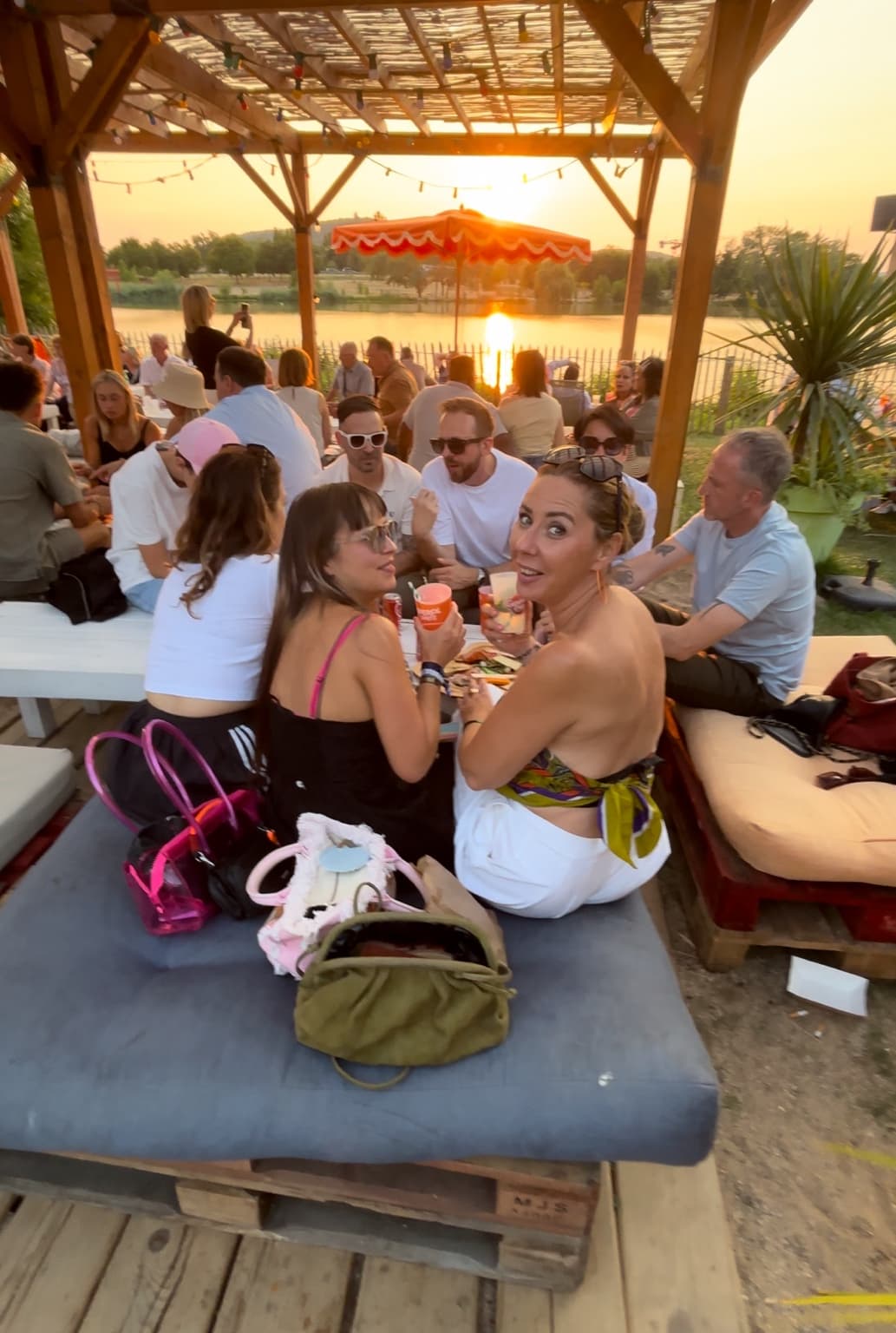 Une tablée d’amis trinque au soleil couchant sous une pergola au bord de l’eau, lors d’une soirée OZ en vrai à Metz.